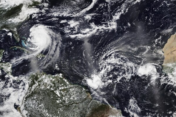 In this Tuesday, Aug. 19, 2025, satellite image released by NASA, Hurricane Erin, left, continues its slow west-northwest trajectory across the Atlantic Ocean, as the National Hurricane Center is watching two more clusters of Cape Verde storms off the west coast of Africa, right, that could develop into tropical storms. (NASA Worldview, Earth Observing System Data and Information System (EOSDIS) via AP)
