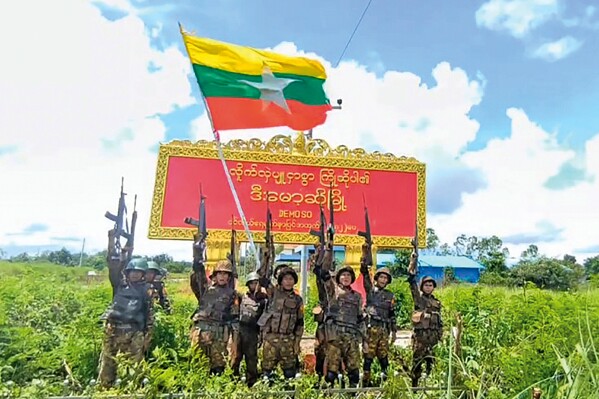 Army soldiers pose in front of the sign for the town of Demoso in Myanmar's eastern state of Kayah, which the military government claimed to have recaptured from resistance forces on Tuesday, Aug. 19, 2025 (Myanmar Military via AP)