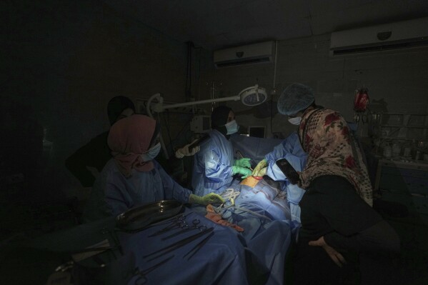 Dr. Abeer Al-Gharbawi performs surgery illuminated by the flashlights of two cellphones during a power outage at Shifa Hospital in Gaza City, July 4, 2025. (AP Photo/Jehad Alshrafi)