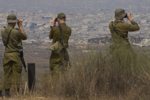 Israeli soldiers uses binoculars to look at damaged buildings in the Gaza Strip, from southern Israel, Wednesday, Aug. 13, 2025. (AP Photo/Ariel Schalit)